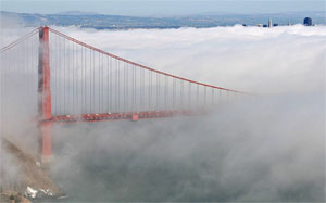 Golden Gate bridge in the forefront under fog with the San Francisco skyline in the background